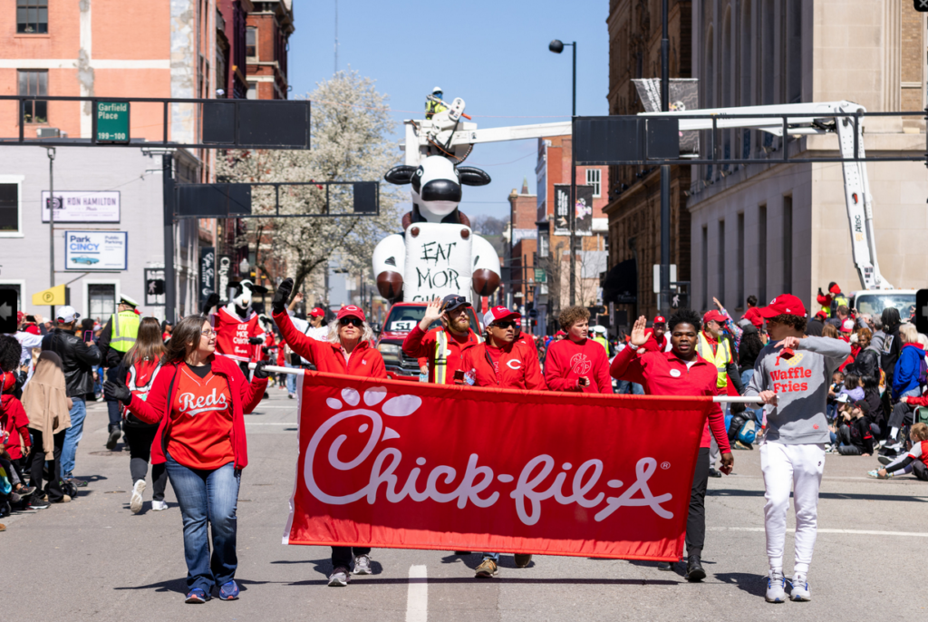 Chick-fil-A marches at the 2026 Findlay Market Opening Day Parade. Team carries banner. 12 ft inflatable in pick-up truck. Cows dance on float. Cows meet kids in the crowd.